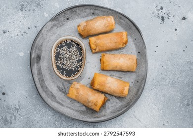 Crispy fried spring rolls served with soy dipping sauce and sesame seeds Asian appetizer flat lay on stone background.