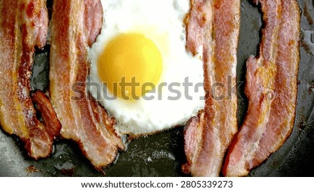 Crispy pork bacon and egg being cooked with Splashes of sizzling oil. Close-Up view of Cooking Bacon and Egg in a frying Pan. Fast and easy breakfast.