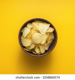 Crispy potato chips in bowl on yellow background, top view