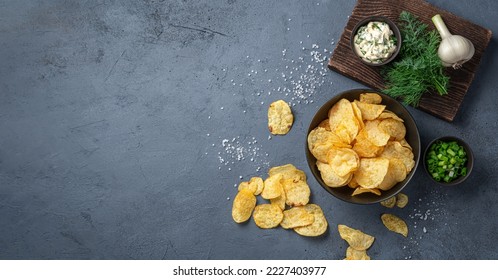 Crispy potato chips with herbs, salt and sour cream on a graphite background. Top view, copy space. - Shutterstock ID 2227403977