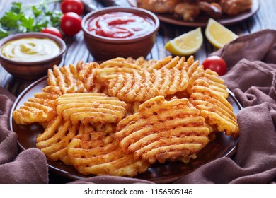 Crispy Potato Criss Cross Fries on a clay plates on a wooden table with mustard and tomato sauce dipping and sticky chicken wings at the background, view from above, close-up