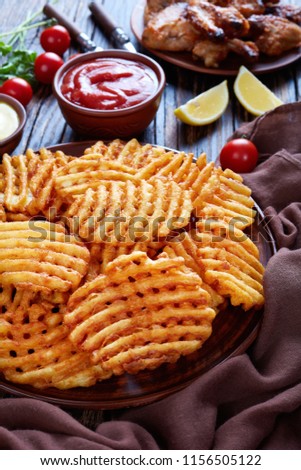 Crispy Potato Criss Cross Fries on a clay plates on a wooden table with mustard and tomato sauce dipping and sticky chicken wings at the background, vertical view from above