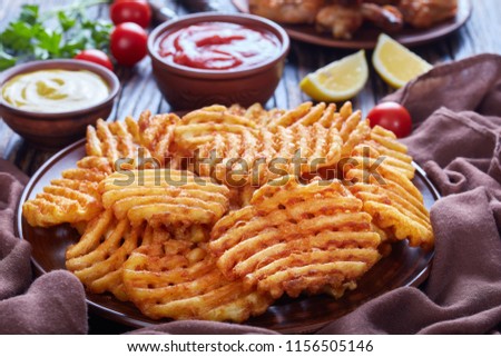 Crispy Potato Criss Cross Fries on a clay plates on a wooden table with mustard and tomato sauce dipping and sticky chicken wings at the background, view from above, close-up