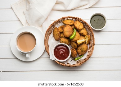 Crispy Potato Pakora OR Aloo Pakoda OR Batata Bhajji served with tomato ketchup, green fried chilly and hot tea, Popular indian all time snack, selective focus