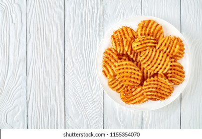 Crispy Potato Waffles Fries, Wavy, Crinkle Cut, Criss Cross Fries on a white plate on a wooden table, view from above, flat lay 