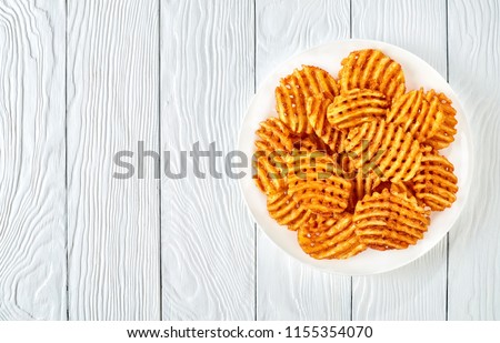 Crispy Potato Waffles Fries, Wavy, Crinkle Cut, Criss Cross Fries on a white plate on a wooden table, view from above, flat lay 