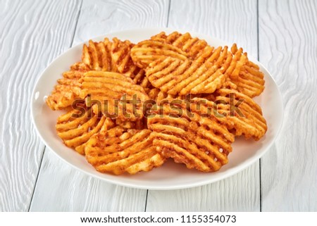 Crispy Potato Waffles Fries, Wavy, Crinkle Cut, Criss Cross Fries on a white plate on a wooden table, view from above, close-up 