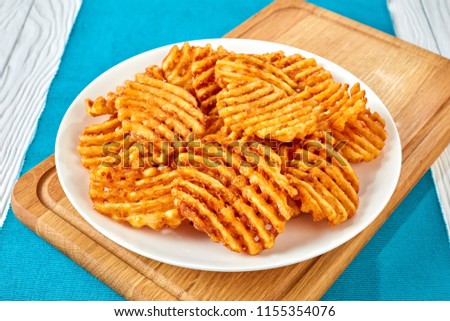 Crispy Potato Waffles Fries, Wavy, Crinkle Cut, Criss Cross Fries on a white plate on a cutting board on a wooden table, view from above, close-up