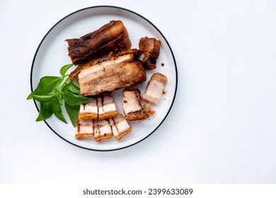 Crispy roast pork, usually the fatty pork belly, served on a white plate with a garnish of fresh basil leaves