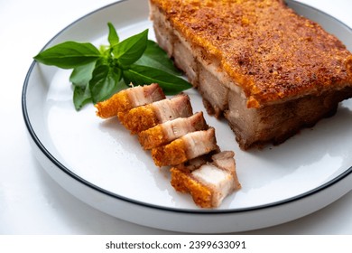 Crispy roast pork, usually the fatty pork belly, served on a white plate with a garnish of fresh basil leaves