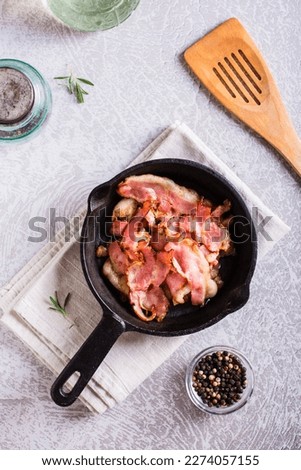 Crispy strips of bacon fried in a pan on the table. Top and vertical view