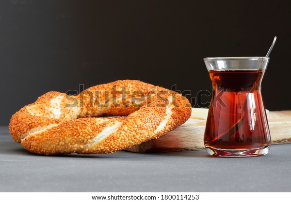 Crispy Turkish traditional bagel / simit with\
sesame and glass of turkish black tea on rustick background,\
turkish breakfast pastry\
concept