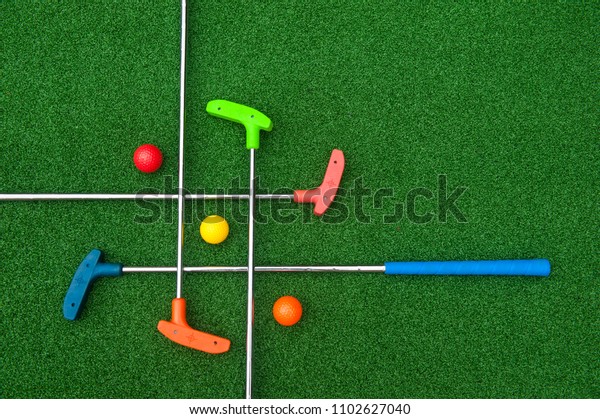 Criss Cross of colorful mini golf clubs and balls\
on artificial grass