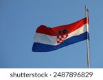 The Croatian flag fluttering in the wind on a flag pole against a clear blue sky