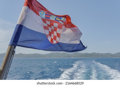 The Croatian flag flutters in the wind, with a ferry trail in the background