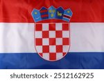 Croatian national flag featuring the coat of arms and colorful symbols against a red, white, and blue fabric backdrop