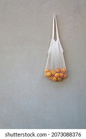 Crochet Bag Filled With Fresh Tangerines, Hanging On A Concrete Wall.