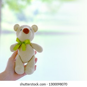 Crochet light brown teddy bear have a green bow tie in hand. Copy space. - Shutterstock ID 1300098070
