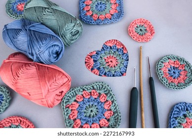 Crochet pattern in a heart and three different hooks with other patterns and skeins of yarn around on grey background. Love to crocheting.