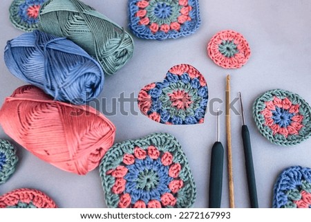 Crochet pattern in a heart and three different hooks with other patterns and skeins of yarn around on grey background. Love to crocheting.