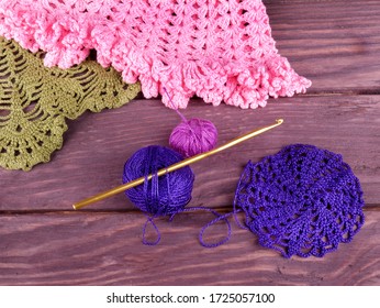Crochet and a skeins of dark blue and pink  yarn, top view on a dark wooden background, in the background in the upper left corner the finished products are partially visible