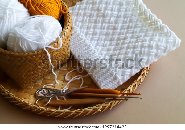 Crochet work with cotton yarn, yarn balls and wood\
crochet needles on threshing basket. Handmade and crochet hat.\
Slouch or beanie hat.
