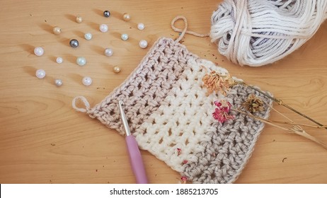 A Crocheted Scarf Pattern In Progress, Made In A Neutral Toned, Chunky, Self Striping Yarn, And Posed With Pearls, Dried Flowers, And A Lavendar Crochet Hook.