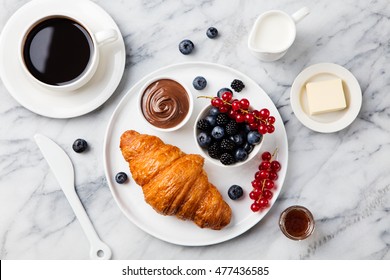 Croissant  with fresh berries, chocolate spread and butter with cup of coffee on a marble texture background. Top view - Powered by Shutterstock