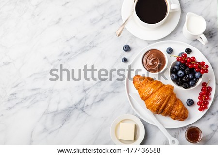 Croissant  with fresh berries, chocolate spread and butter with cup of coffee on a marble texture background. Top view Copy space