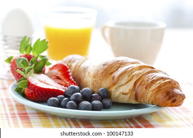 Croissant, fresh strawberries and blueberries, coffee, orange juice and an egg for healthy breakfast
