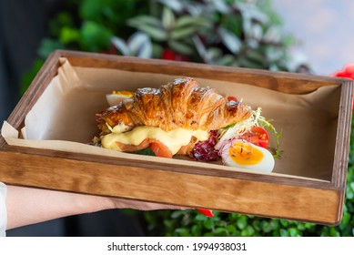 croissant sandwich stuffed with cold smoked salmon and hollandaise sauce served on wooden tray