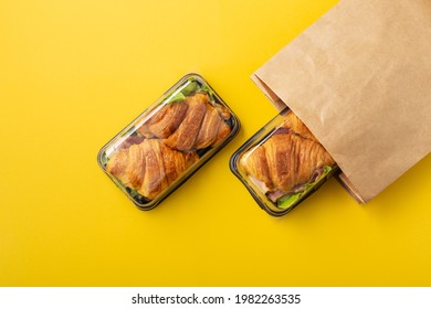 Croissant Sandwich In Takeaway Or Delivery Food Container And Paper Bag On Yellow Background, Top View