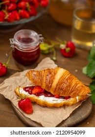 Croissant stuffed with curd cheese, strawberries and strawberry jam lying on a wooden board