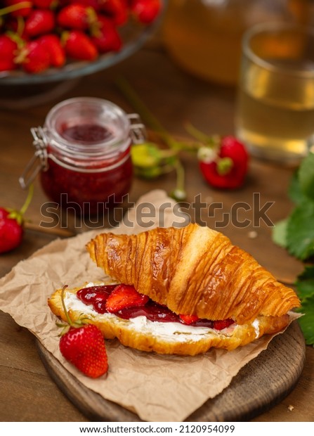 Croissant stuffed with curd cheese,\
strawberries and strawberry jam lying on a wooden\
board