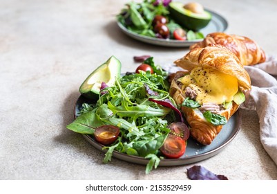 Croissant with tuna, poached egg, avocado and hollandaise sauce served with salad leaves and tomatoes. Croissant sandwich with egg benedict and tuna.