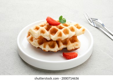 Croissant Waffle or Croffle with strawberry and mint leaf topping served in white plate and grey background. Close up, copy space.