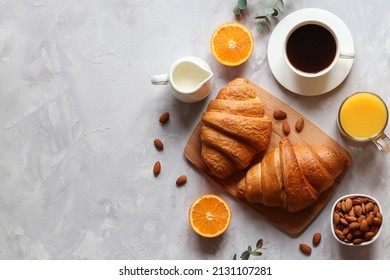 Croissants with orange juice, orange fruit, coffee with milk and almond nuts on the table. French or continental breakfast. Selective focus, top view and copy space.