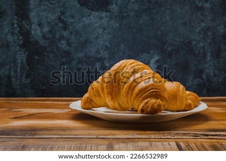 Croissants in white plate on wooden table. Side view.