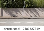 Crooked road sign pole on sidewalk. Light brown plaster fence with trees on behind.street in front. Background for copy space.