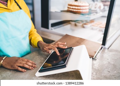 Crop African American female in apron touching screen of modern tablet while standing behind counter of small cafe and working - Powered by Shutterstock