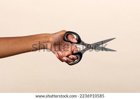 Crop anonymous African American female showing metal scissors on beige background in studio