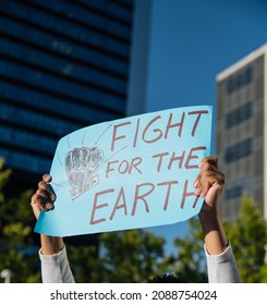 Crop anonymous African American person raising arms and demonstrating placard with inscription fight for the earth while standing on street in city in sunny day - Shutterstock ID 2088754024