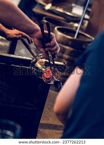 Crop anonymous craftsmen working with hot glass and creating glass bottle fixed on metal bar and using professional tool in glass factory