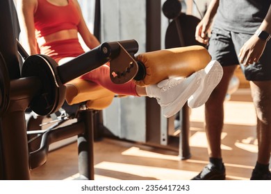 Crop anonymous female athlete doing leg extension on machine during workout with black coach in gym on sunny day