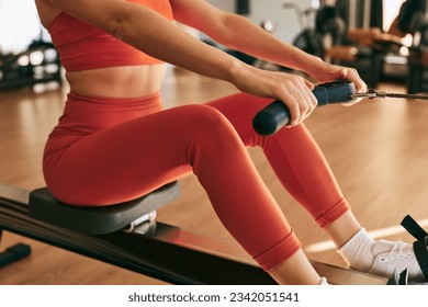 Crop anonymous female athlete in tight orange sportswear doing exercise with resistance band on rowing machine during workout in gym - Powered by Shutterstock