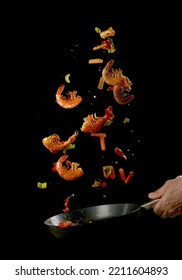 Crop anonymous male chef tossing food in frying pan while preparing delicious prawns and vegetables against black background - Shutterstock ID 2211604893