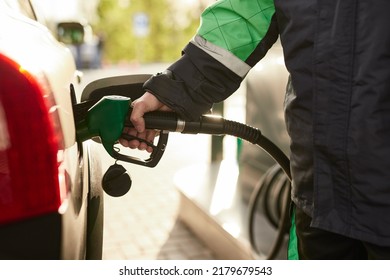 Crop anonymous male employee in protective uniform pouring fuel into tank of modern car while working in gas station on sunny day - Shutterstock ID 2179679543