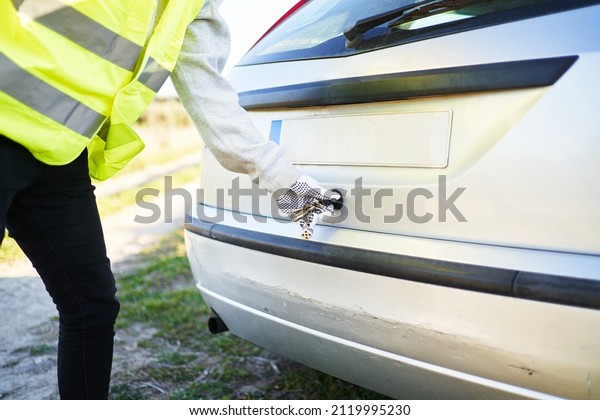 Crop anonymous male in warn vest and protective glove\
opening trunk of modern automobile parked in countryside on summer\
day