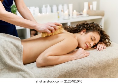 Crop anonymous master doing body dry brush massage with brush to topless female client during skin care procedure in modern spa salon