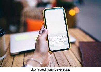 Crop Anonymous Woman Sitting At Wooden Table With Laptop And Coffee While Texting Message On Modern Mobile Phone On Cafe Terrace